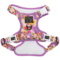 Adjustable dog harness with a floral pattern in pink, purple, and yellow colors, featuring white straps and a metal d-ring.